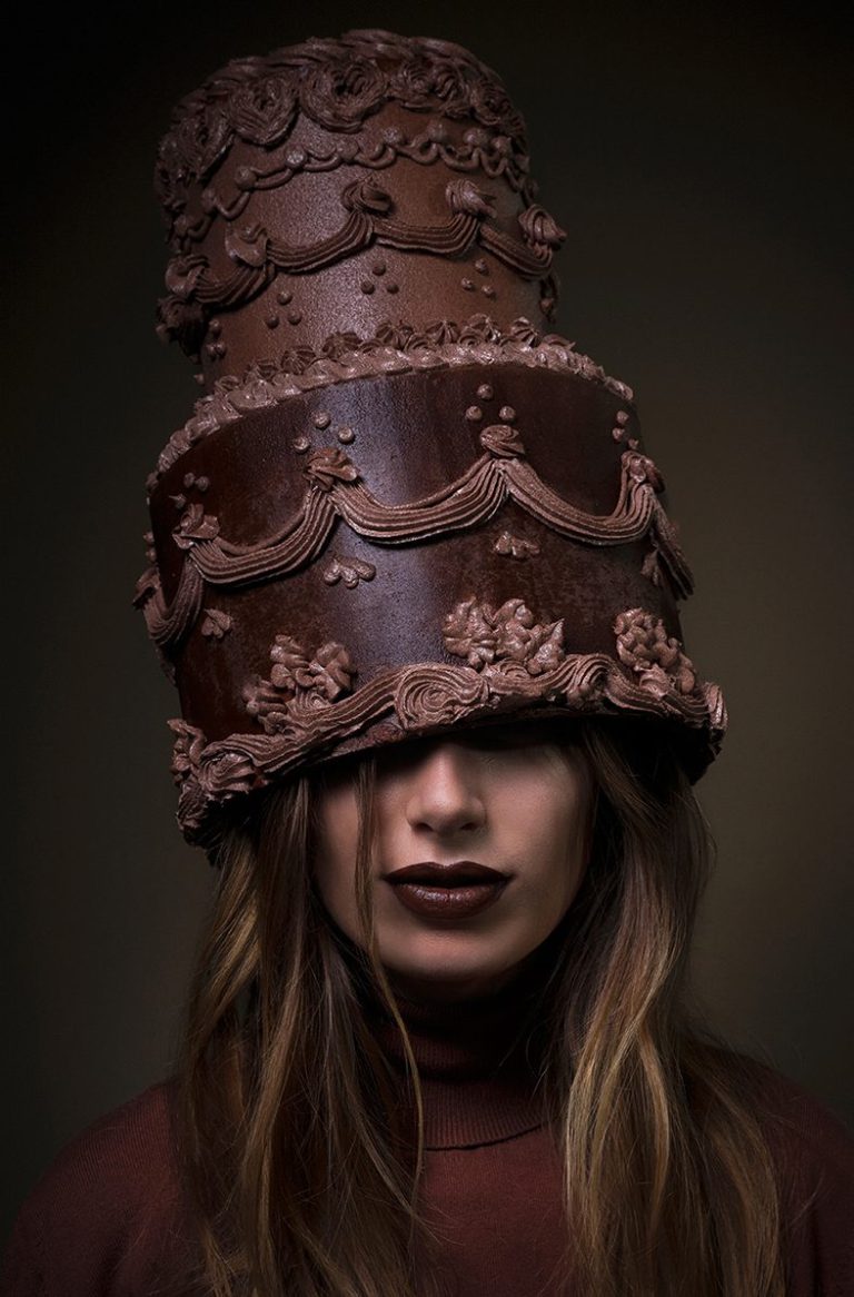 Fine art portret van een langharige brunette getooid met een in barokstijl gedecoreerde hoge chocolade taart